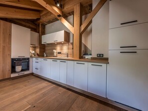 Eine moderne Küche mit Holzbalken, weißen Schränken, einem eingebauten Ofen und einer Holz Arbeitsplatte.
