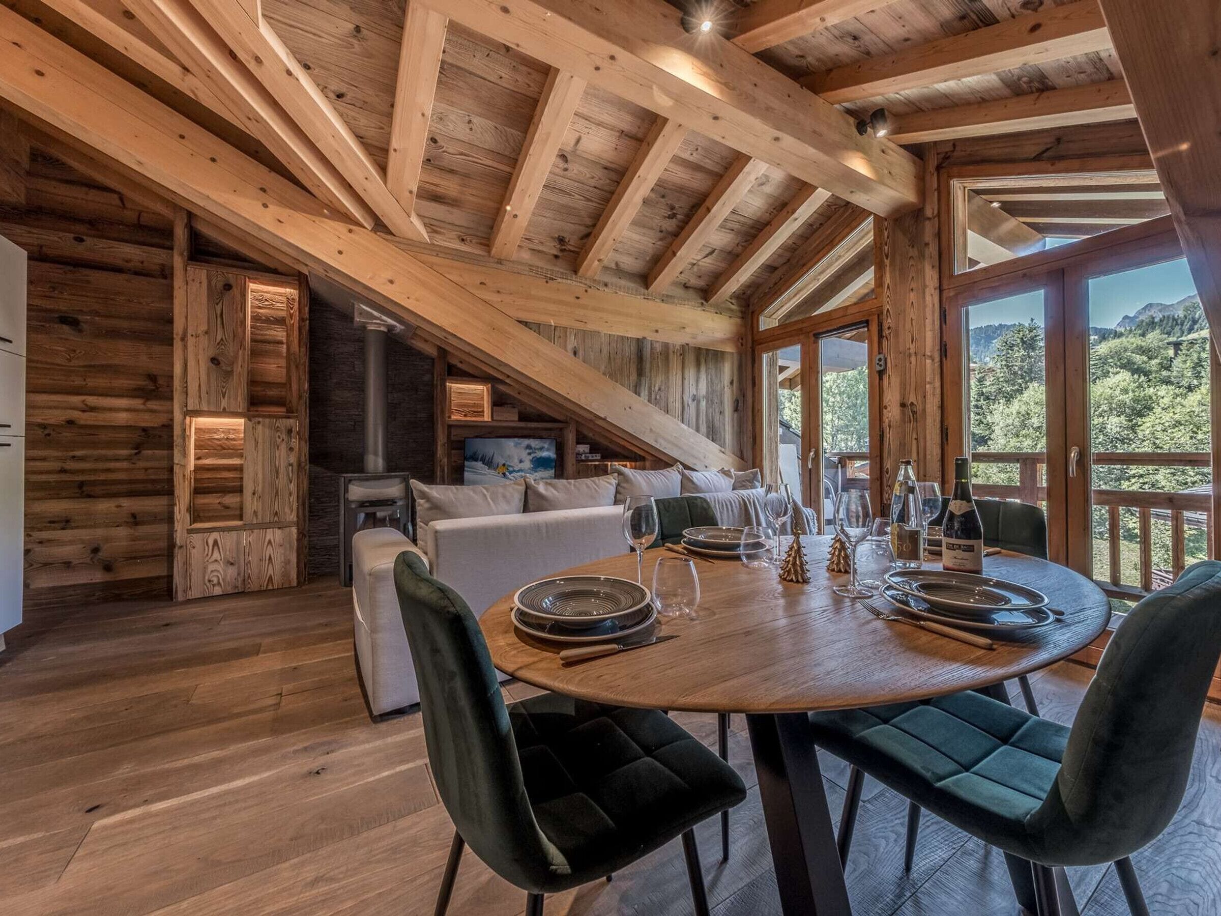 A wooden cabin interior with a dining area, sofa, and a TV.