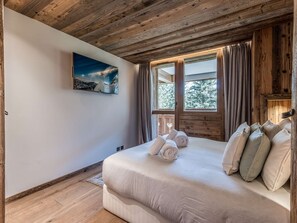 Ein Schlafzimmer mit Holzbalkendecke, einem Bett mit Kissen und Handtüchern, einem Fenster mit Vorhängen und einem Bild an der Wand.