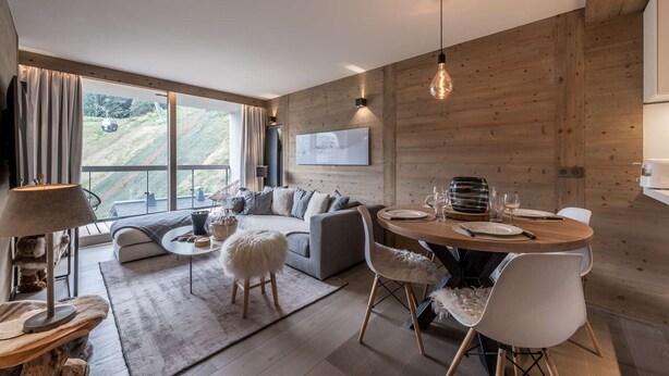 A modern living room with a sofa, coffee table, and dining area with chairs and a table set for two. - Modern apartment Courchevel 1550, 4 people, parking, wifi (Courchevel)