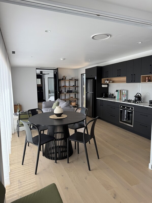 A modern kitchen with dark cabinets, a built-in oven, and a dining area with a round table and chairs.