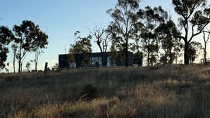 A modern building with a flat roof, surrounded by trees and grassy terrain.