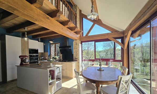 A spacious kitchen with a central island, a dining area with a round table, and large windows offering a view of the outdoors. - Perigord house, pool, pets allowed (Jumilhac-le-Grand)