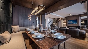 Un espace de repas moderne avec une longue table en bois dressée pour le repas, un canapé et un téléviseur en arrière-plan.