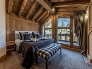 A bedroom with a large bed, wooden ceiling beams, a bench, and a view of the outdoors. - Courchevel 1850: Ski-in/ski-out apartment, 3 bedrooms, Wi-Fi, parking (Courchevel)