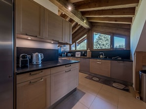 A modern kitchen with wooden cabinets, a black countertop, and a window with a view of trees. - Courchevel 1850: Ski-in/ski-out apartment, 3 bedrooms, Wi-Fi, parking (Courchevel)