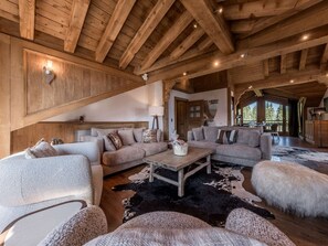 A spacious living area with a high wooden ceiling, a fireplace, and a large window offering a view of the outdoors. - Courchevel 1850: Ski-in/ski-out apartment, 3 bedrooms, Wi-Fi, parking (Courchevel)