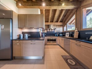 A modern kitchen with wooden cabinets, a stainless steel refrigerator, a built-in oven, and a large window providing natural light. - Courchevel 1850: Ski-in/ski-out apartment, 3 bedrooms, Wi-Fi, parking (Courchevel)