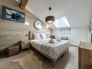 Een slaapkamer met een bed, een ronde spiegel, een houten hoofdbord, een klein kistje, een vachtkleed, een hanglamp en een dakraam.