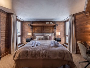 Ein Schlafzimmer mit einem großen Bett, zwei Nachttischen mit Lampen, Holzwänden und Blick durch das Fenster.