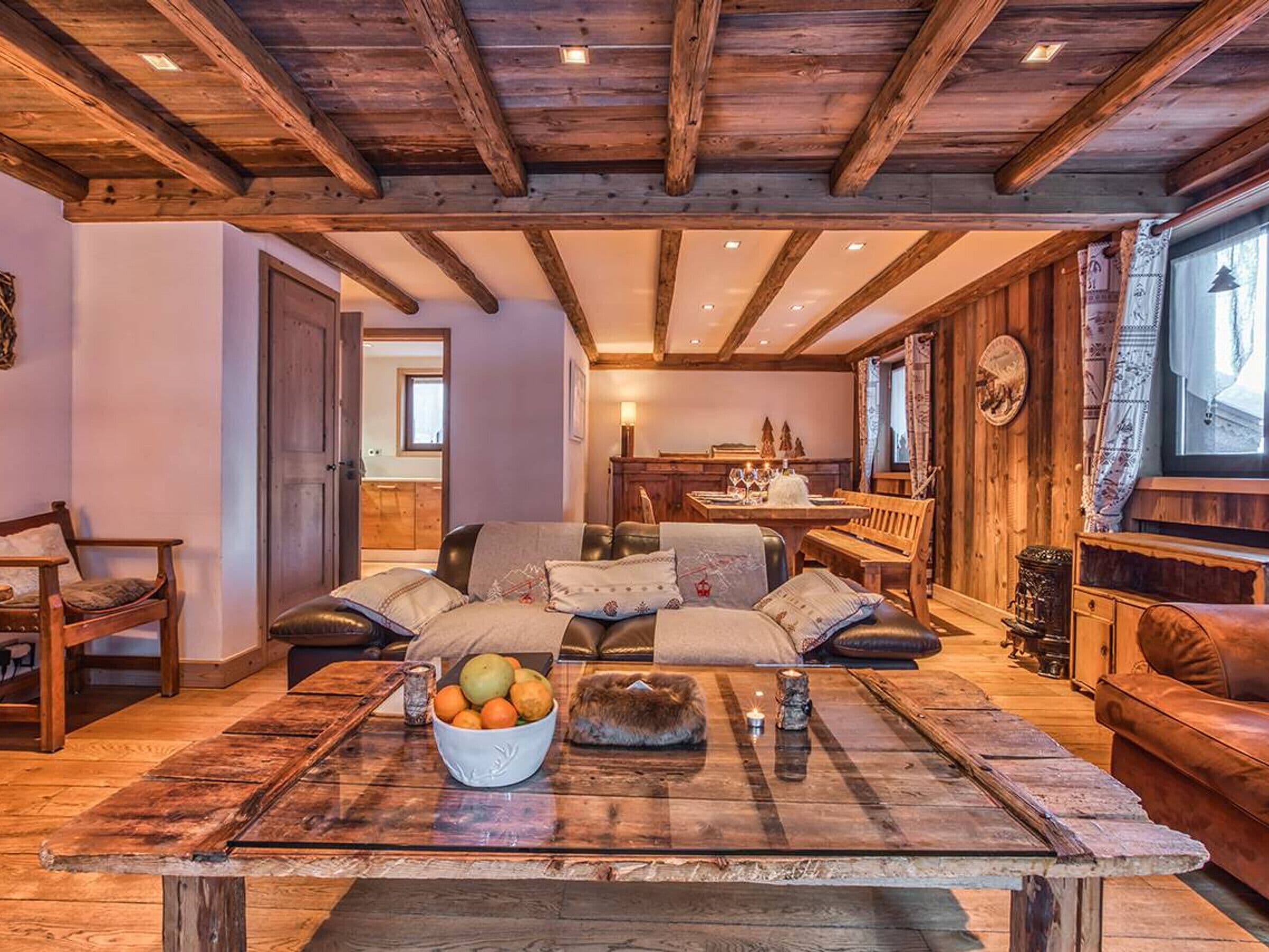 A rustic interior with a wooden ceiling, a dining area, and a seating area with a table and cushions.
