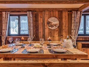 Ein Holzespeisetisch ist mit Tellern, Gläsern und Kerzen gedeckt, im Hintergrund eine Holzvertäfelung und Fenster.