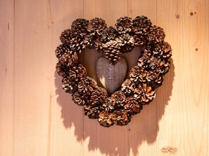 Une couronne en forme de cœur, faite de pommes de pin, est accrochée à un mur en bois.