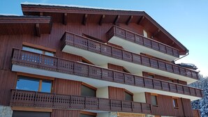 A multi-story wooden building with balconies, stone foundation, and a sign indicating 'Residence Le Rocher'. - Studio Courchevel 1850 - Sleeps 4 - Ski-in/Ski-out with covered parking (Courchevel)