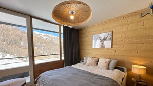 Camera da letto con un letto grande, una parete in legno, una finestra vista su un paesaggio innevato e una lampada a sospensione.