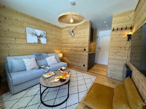 Ein gemütliches Zimmer mit einer Couch, einem Tisch mit Essen, einer Hängelampe und Holzwänden.