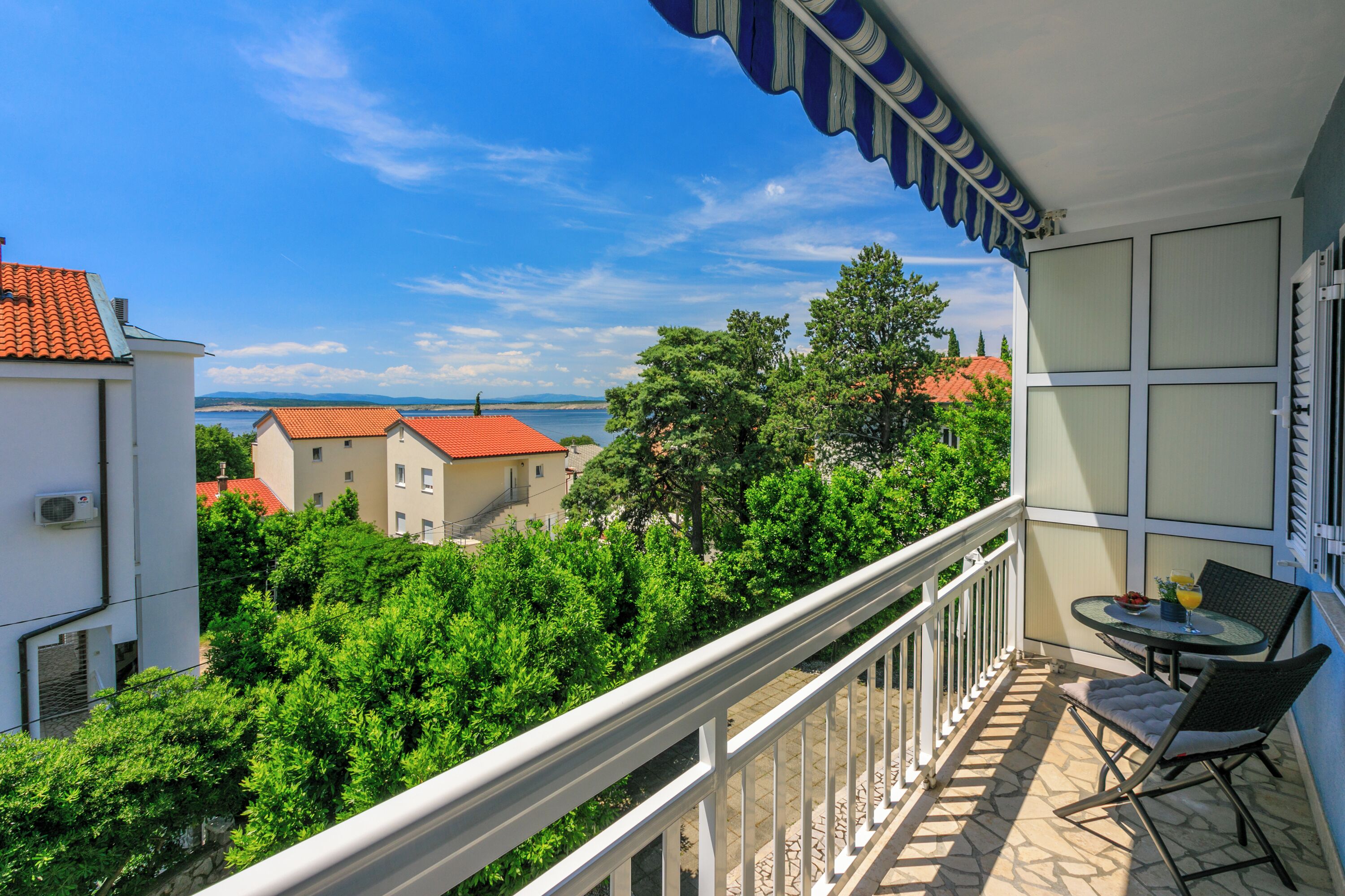A balcony with a view of the sea, a table with chairs, and a railing.