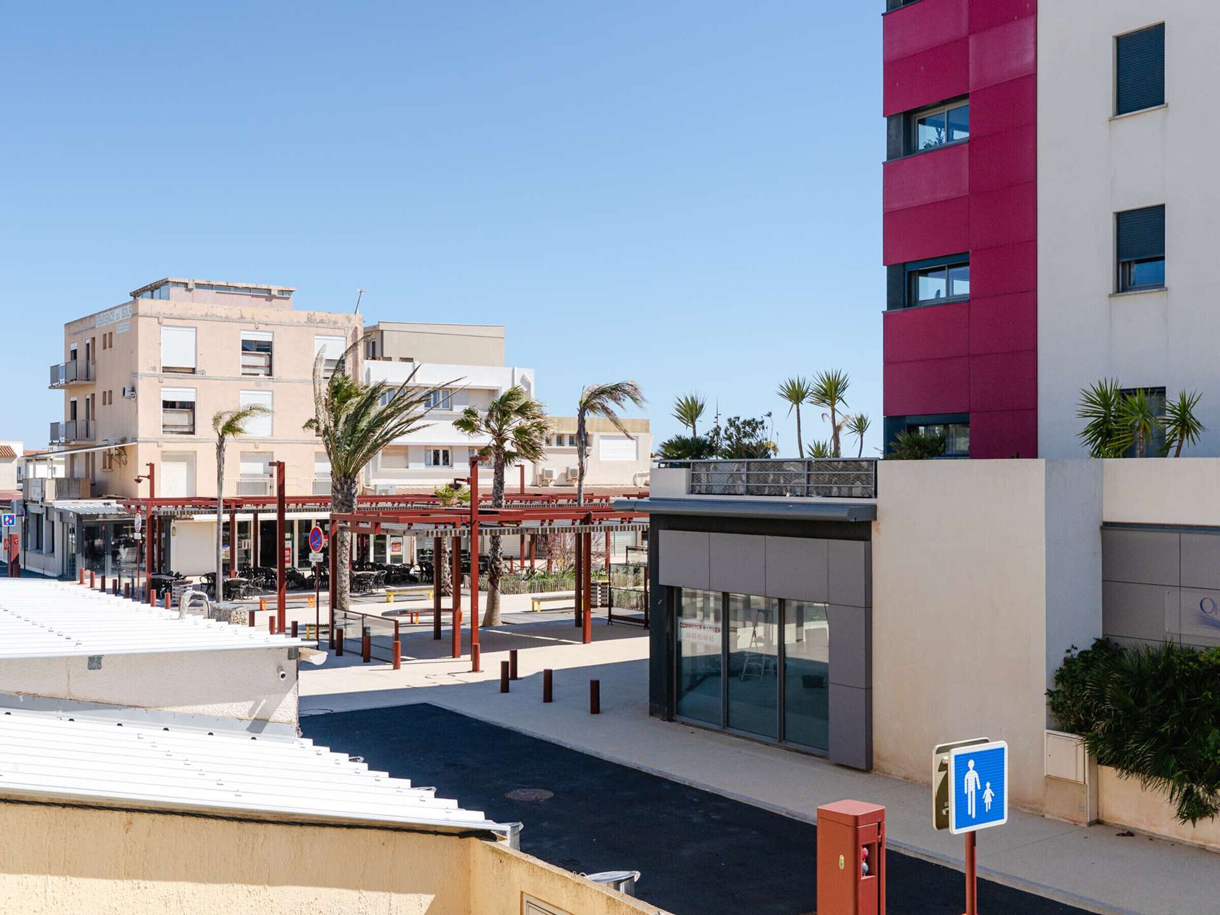 A modern building with a red and white facade, a covered pedestrian walkway, and palm trees.