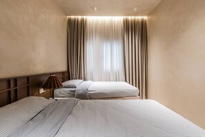 A hotel room with two beds, a nightstand, and a window with curtains.