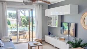 Un salon moderne avec un canapé, une table basse, un téléviseur et un balcon équipé de chaises.