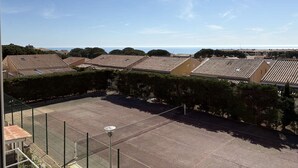 Ett bostadsområde med hus som har tak av terrakottafärgat tegel, en tennisbana omgiven av ett staket och en klar himmel.