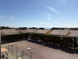 Ein Wohngebiet mit Häusern mit Terrakotta-Dächern, einem eingezäunten Tennisplatz und blauem Himmel.