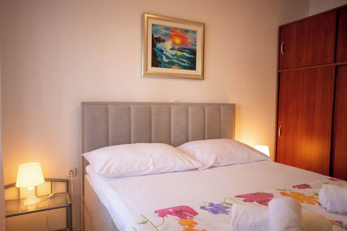 Una camera d'albergo con un letto, un comodino con una lampada, un armadio in legno e un quadro appeso al muro.