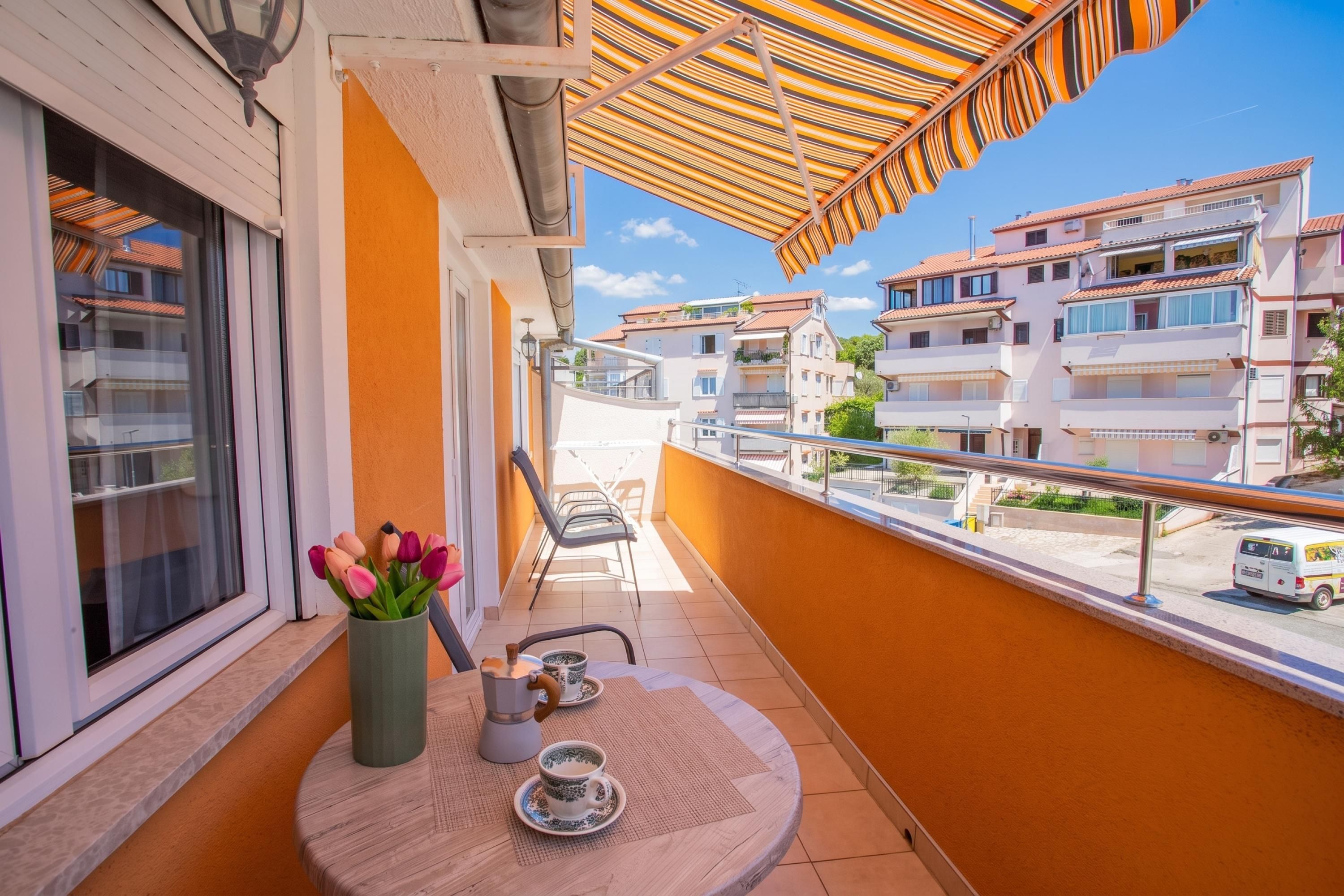 A balcony with a table, chairs, and a view of neighboring buildings.