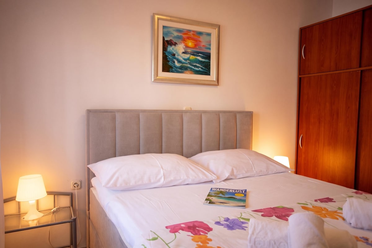 A hotel room with a bed, a nightstand, a lamp, a framed picture on the wall, and a wooden wardrobe.