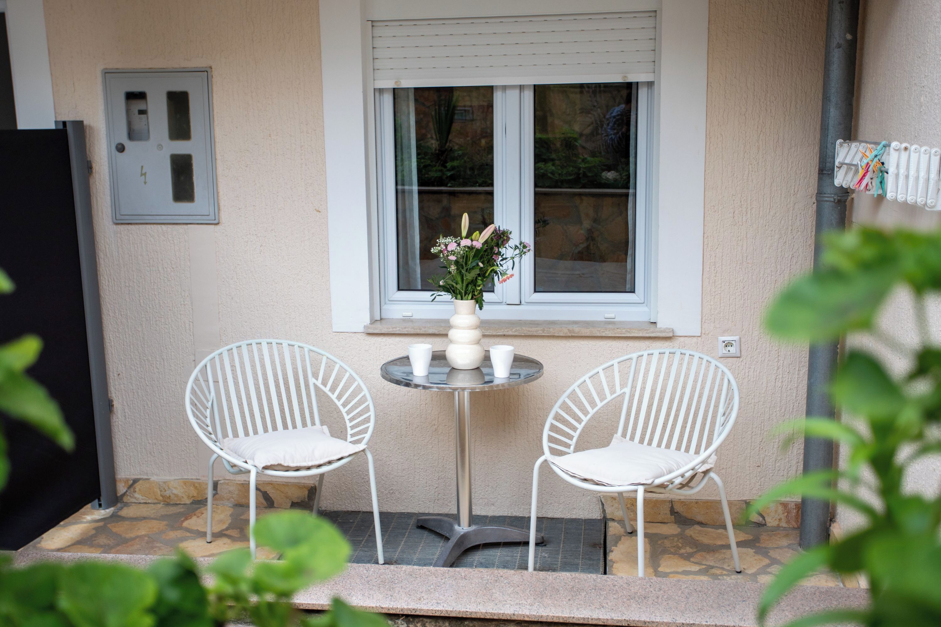 Een terras met twee witte stoelen, een klein rond tafeltje en een vaas met bloemen.