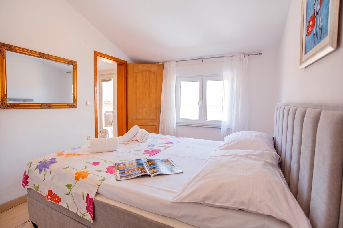 A bedroom with a bed, a window, a door, and a mirror.