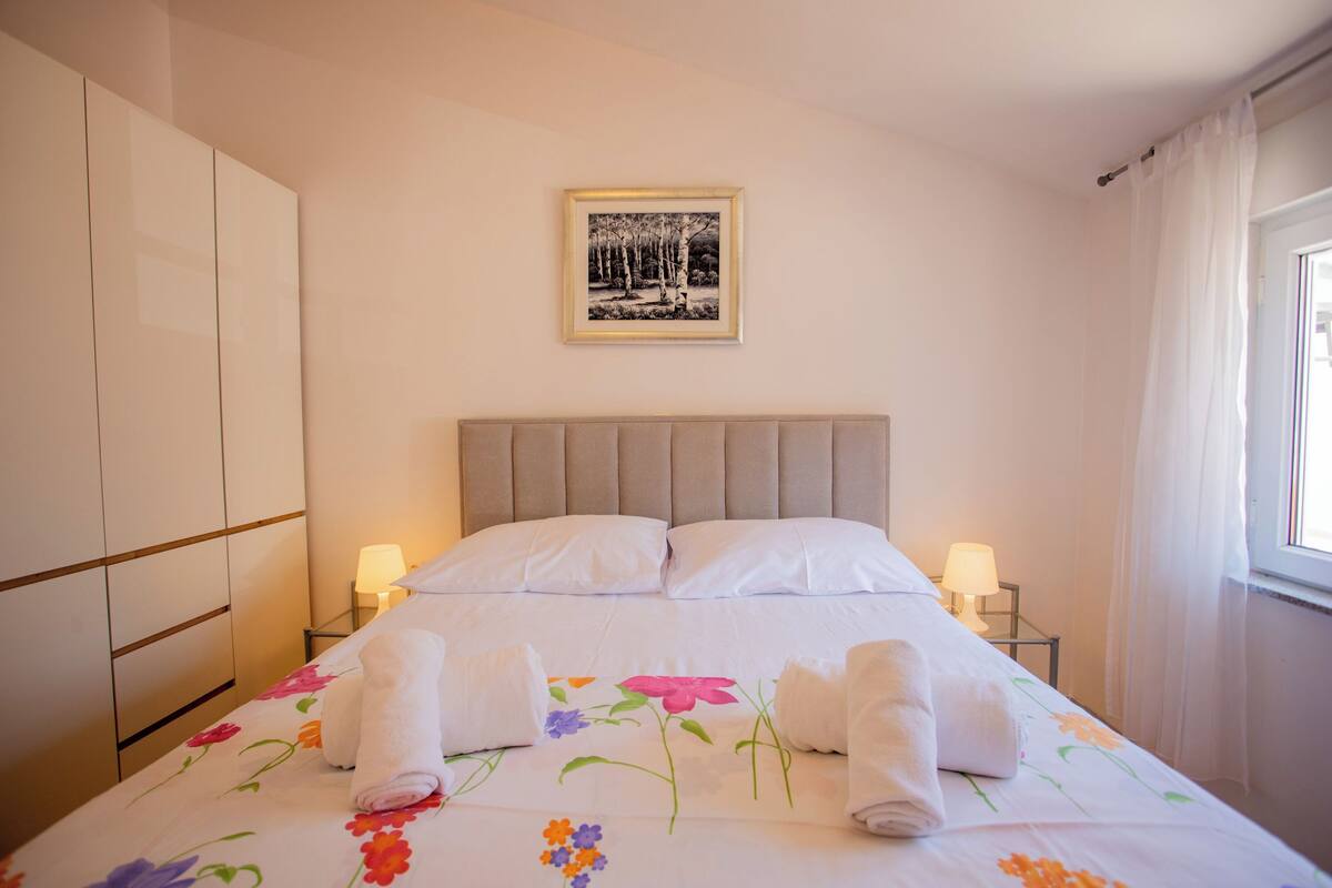 Una camera d'albergo con un letto, una testiera, un comodino con una lampada, un armadio e un quadro appeso al muro.