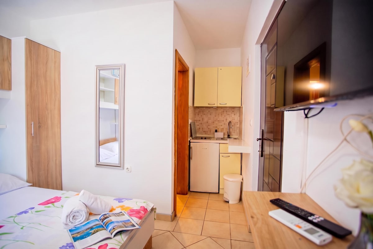 A hotel room with a bed, a small kitchenette, and a TV.