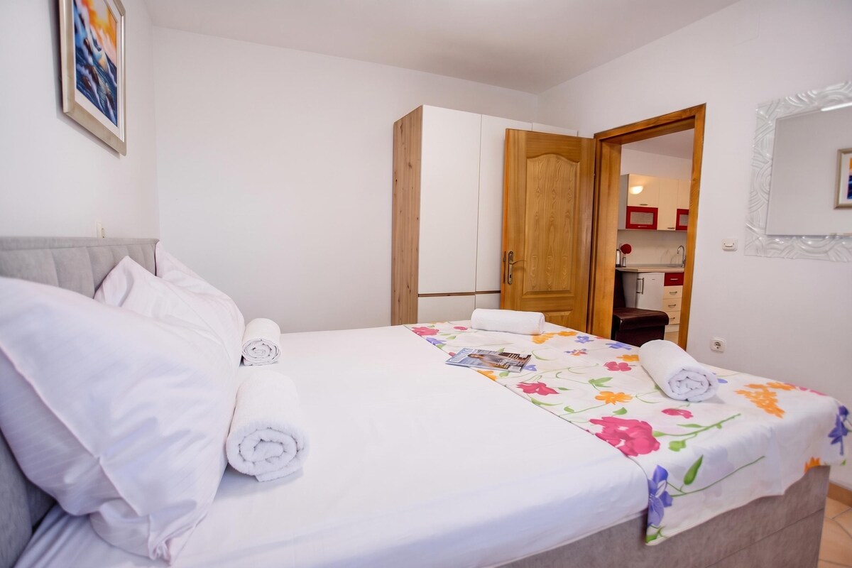 A hotel room with a bed, a wooden door, a small kitchenette, and a mirror on the wall.