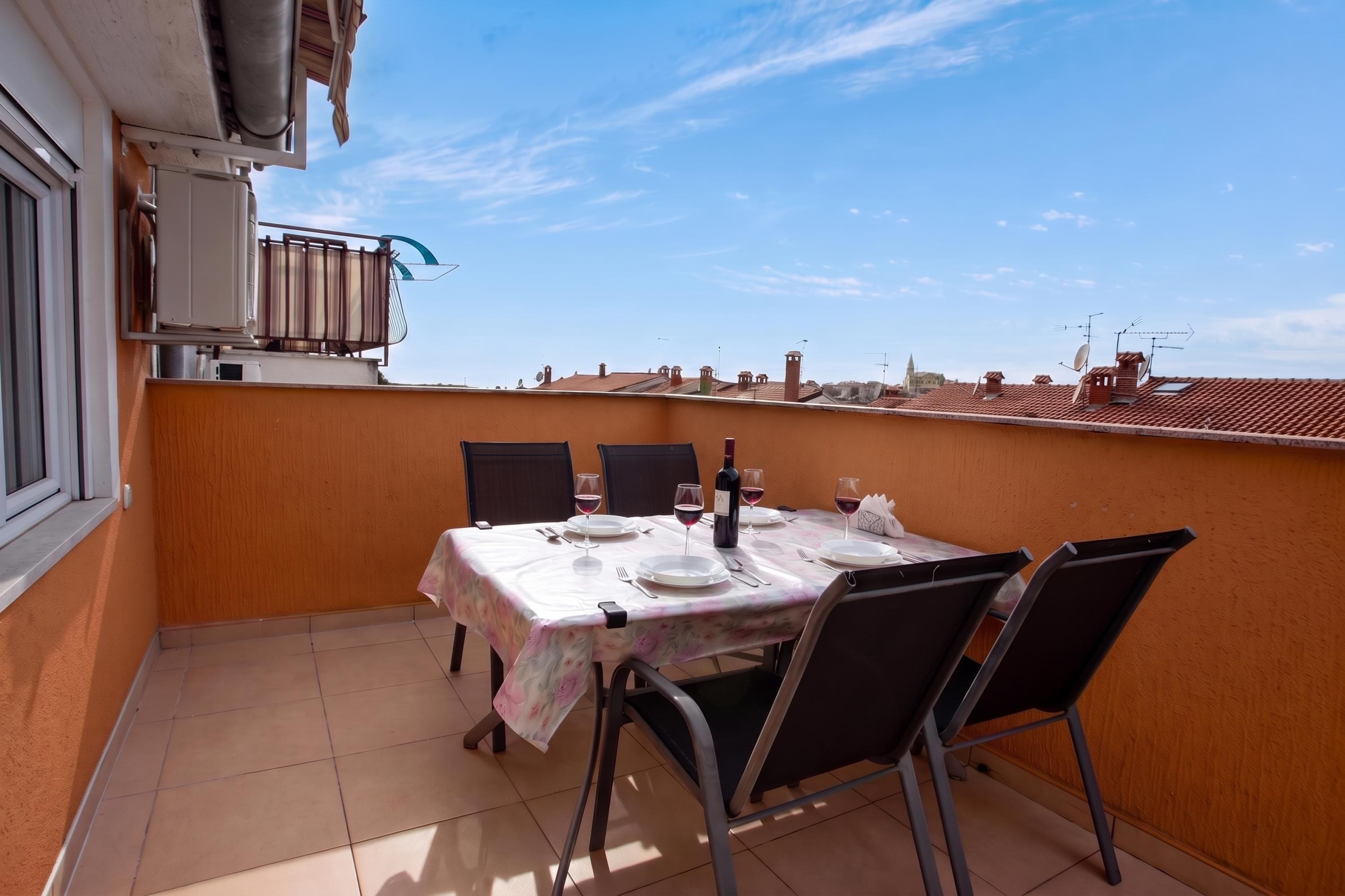 A balcony with a table set for two, chairs, and a bottle of wine.