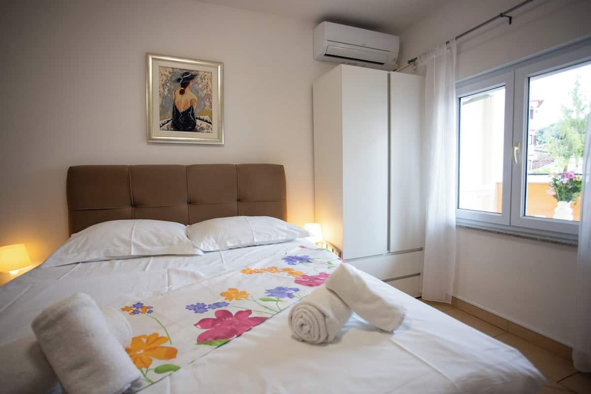Camera d'albergo con un letto, un quadro appeso al muro, un condizionatore d'aria e una finestra con tende.