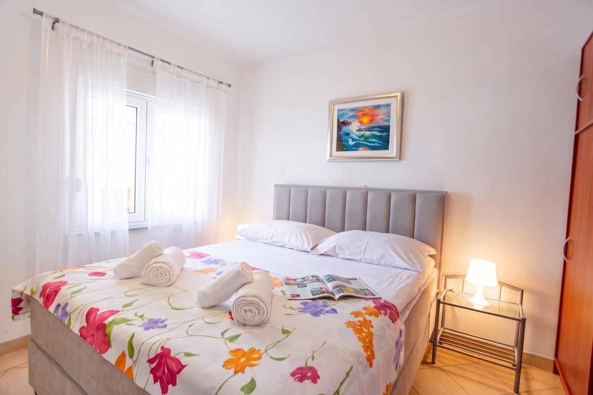 A hotel room with a bed, a nightstand, a lamp, a painting, and a window with curtains.
