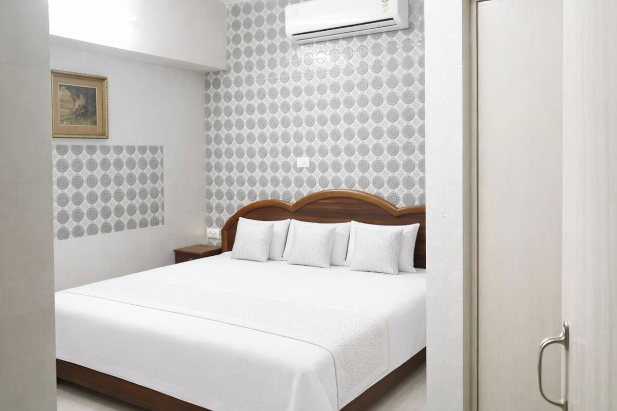 A neatly made bed in a hotel room with a patterned wall, a nightstand, and a door.