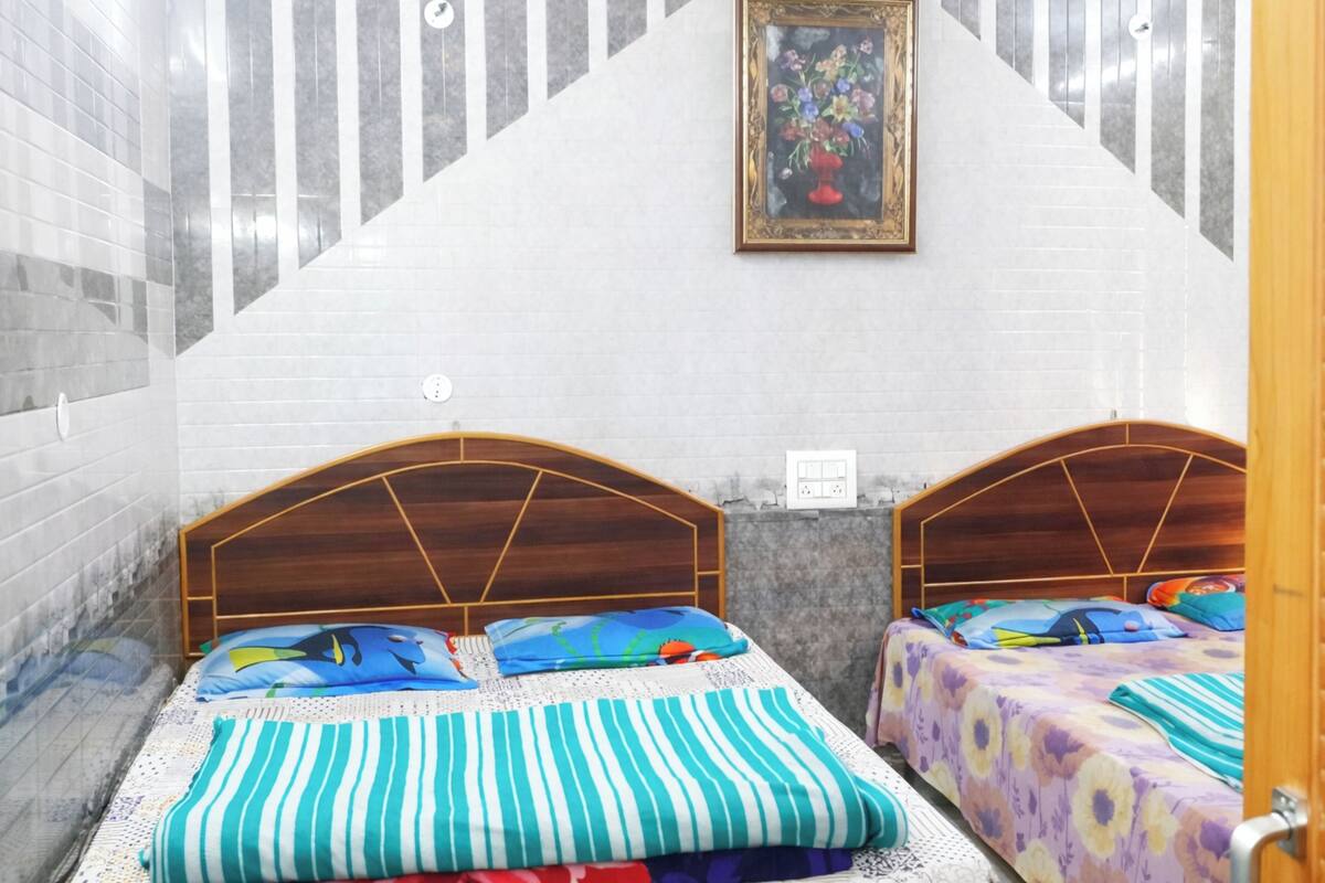 A room with two wooden beds, a white tiled wall, a painting, and a small window.