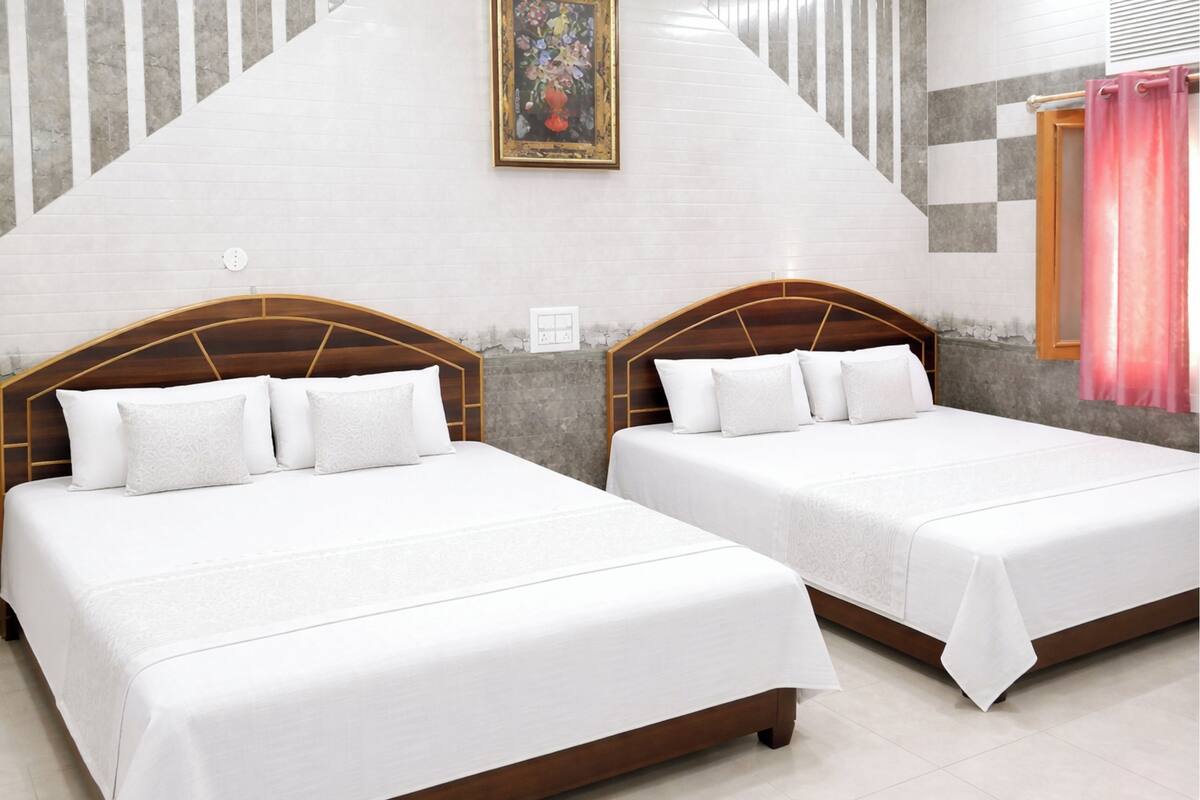 Two double beds with wooden headboards, a painting on the wall, and a checkered window blind.