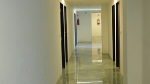 A long, narrow hallway with a shiny floor, white walls, and doors on both sides. - HOTEL KRISHNA INN (Ahmedabad)
