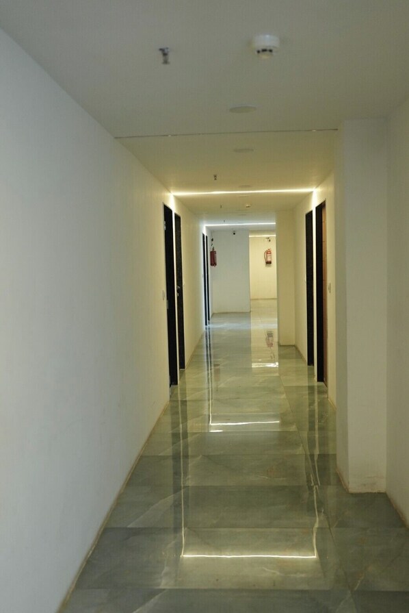 A long, narrow hallway with a shiny floor, white walls, and doors on both sides.