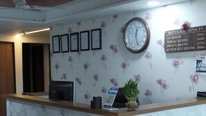 A hotel reception desk with a clock, framed certificates, and a room rate sign. - HOTEL KRISHNA INN (Ahmedabad)