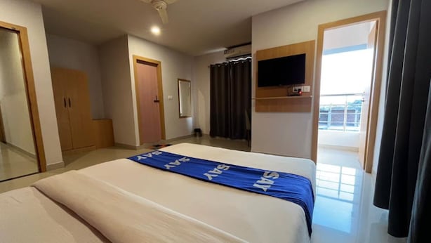 A hotel room with a bed, a television, a door, and a window. - Surbhi Grant (Khatoo)