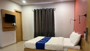 A hotel room with a bed, a TV mounted on the wall, a curtain, and a door. - Surbhi Grant (Khatoo)