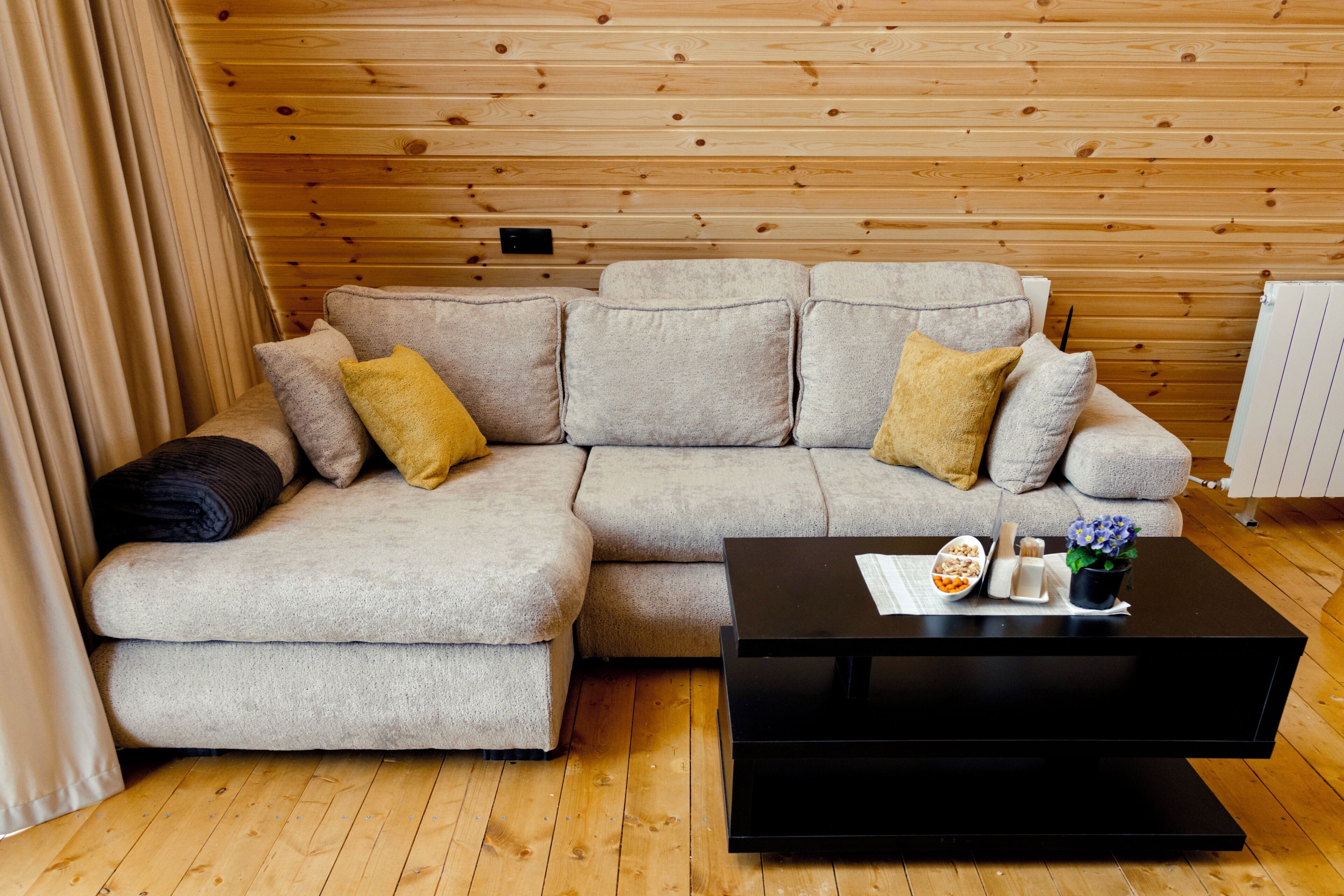 A cozy room with a sectional sofa, a black coffee table, and wooden paneling on the ceiling.