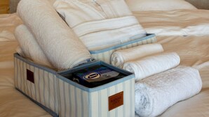Een net opgemaakt bed met handdoeken, een kussen en een verzorgingsset in een kamer met houten wanden en een puntdak.