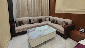 A modern living room with a sectional sofa, a marble coffee table, and a wooden nightstand. -  Shri Khatu Shyam Residency (Varanasi)