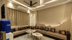 A modern living room with a sofa, two coffee tables, a ceiling fan, and an air conditioning unit. -  Shri Khatu Shyam Residency (Varanasi)