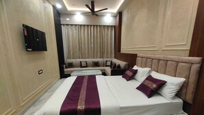 A hotel room with a bed, a sofa, a ceiling fan, and a TV mounted on the wall. -  Shri Khatu Shyam Residency (Varanasi)